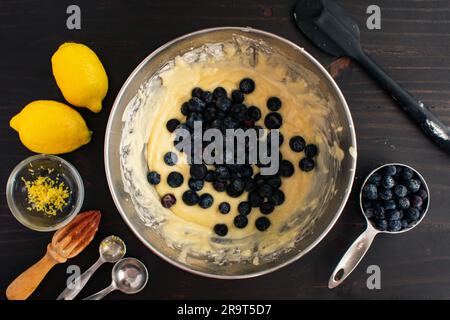 Mixing Bowl Filled with Muffin Batter and Fresh Blueberries: Bowl of blueberry muffin batter surrounded by fresh ingredients and kitchen utensils Stock Photo