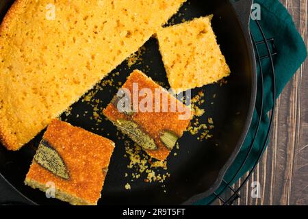 Sage Cornbread Cut Into Pieces in a Cast-Iron Skillet: Freshly baked Southern buttermilk cornbread in a frying pan with butter and honey on the side Stock Photo