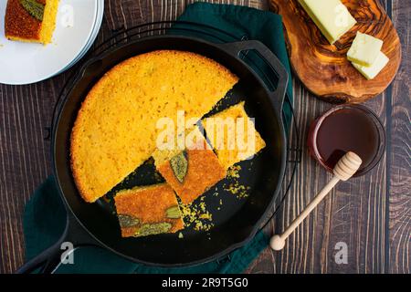 Sage Cornbread Cut Into Pieces in a Cast-Iron Skillet: Freshly baked Southern buttermilk cornbread in a frying pan with butter and honey on the side Stock Photo