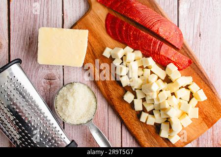 Prepped Pepperoni, Mozzarella, and Parmesan Cheese on a Wooden Background: Sliced pepperoni with chopped and grated cheese and a box grater Stock Photo
