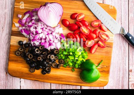 Bell Pepper, Grape Tomatoes, Red Onion, and Black Olives on a Cutting Board: Chopped and sliced vegetables on a carving board with a santoku knife Stock Photo