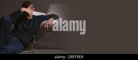 Suffering from hangover. Man with alcoholic drink on floor indoors, space for text. Banner design Stock Photo