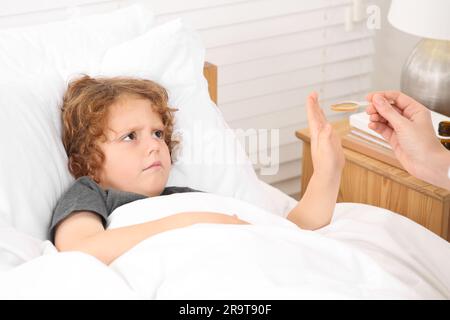 Son refusing to take cough syrup from his mother in bedroom Stock Photo
