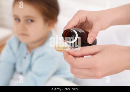 Mother pouring cough syrup into measuring spoon for her daughter indoors, focus on hands Stock Photo