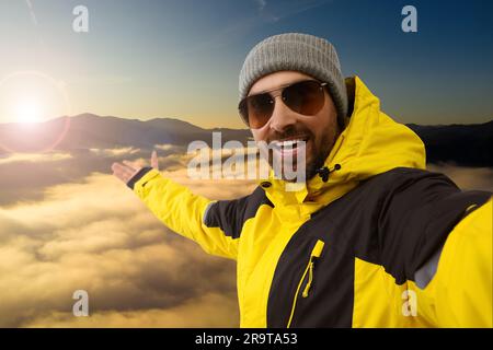 Smiling man in hat and sunglasses taking selfie in mountains Stock Photo