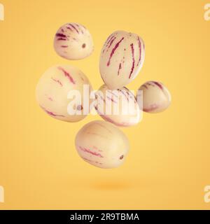 Fresh ripe pepino melons falling on pale orange background Stock Photo