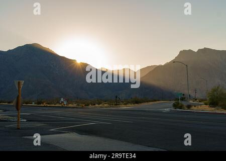 Sun setting over a hill with a beam of light stretching across an intersection Stock Photo