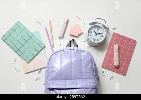 Lilac school backpack with notebooks, alarm clock and markers on white background Stock Photo