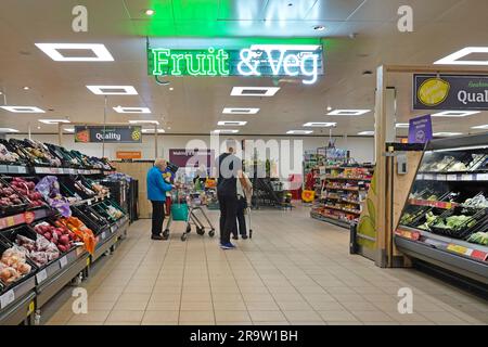 Interior view of customers shopping in Fruit & Veg department of Sainsburys supermarket retail grocery store with illuminated sign Essex England UK Stock Photo