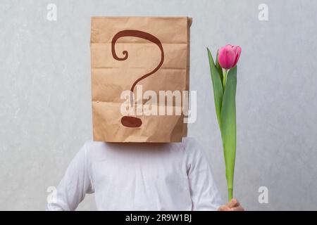 An anonymous man with a box on his head that limits his identity holds a flower. Hidden emotions. A gift from a stranger. Stock Photo