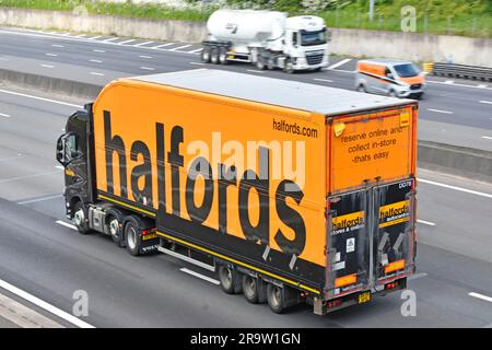 Halfords retail business black Volvo prime mover hgv truck towing rigid body articulated semi trailer orange brand name advert panel UK motorway road Stock Photo