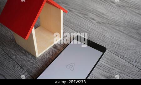 Airbnb logo on smartphone and miniature house on wooden table with copy space Stock Photo