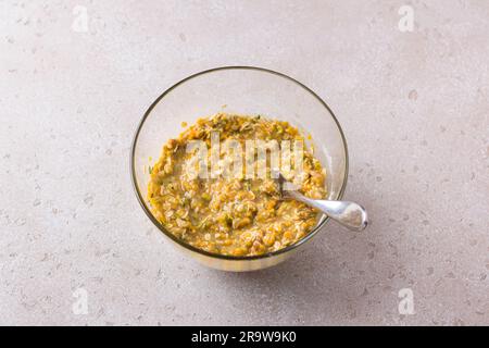 Glass bowl with pumpkin muffin dough with oatmeal, nuts and cinnamon on a beige textured background. Cooking delicious homemade autumn pastries. Stock Photo