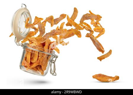Flying dried fruits. Dried mango slices fly out of a glass container on a white isolated background. Mango slices of different sizes scatter to the Stock Photo