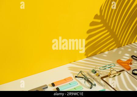 Stationary flat lay on yellow and white background with palm leaf shadow. Stock Photo
