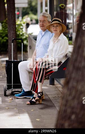 Older couple dressed in summer clothes with a trolley waiting for a bus at a bus stop, Cologne, North Rhine-Westphalia, Germany Stock Photo