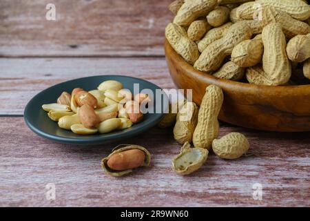 Peanuts in a wooden bowl with peeled peanuts and butter on a spoon Stock Photo