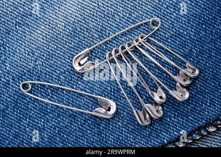 Several safety pins on a blue jeans denim fabric Stock Photo