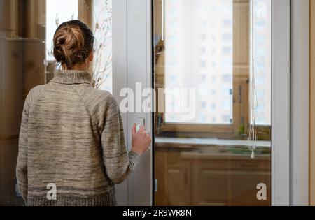 A woman is looking the city through the window during a sad winter day Stock Photo