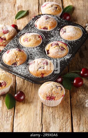 Muffins with cherries and powdered sugar closeup in the muffin mold on the table. Vertical Stock Photo