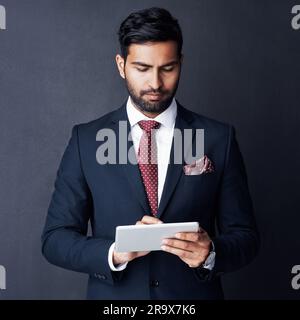 Serious, business man and tablet in studio, dark background and app for trading, planning or internet research. Corporate broker, indian male trader Stock Photo
