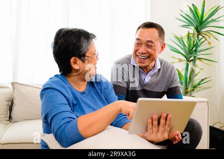 Portrait of healthy senior man and woman using laptop together on sofa at home, Happy senior married couple spending time in living room, Grandparents Stock Photo