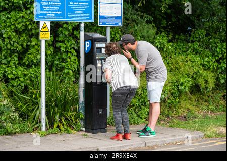 People paying for parking in a car park at a pay and display ticket machine. Paying to park, buying parking ticket. In England, UK. Stock Photo