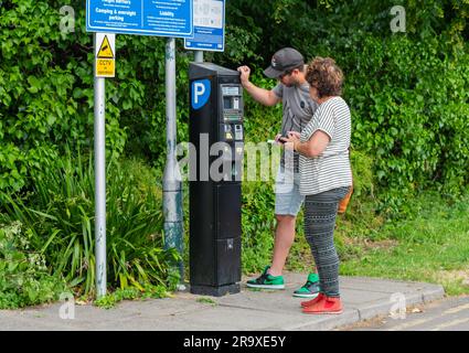 People paying for parking in a car park at a pay and display ticket machine. Paying to park, buying parking ticket. In England, UK. Stock Photo