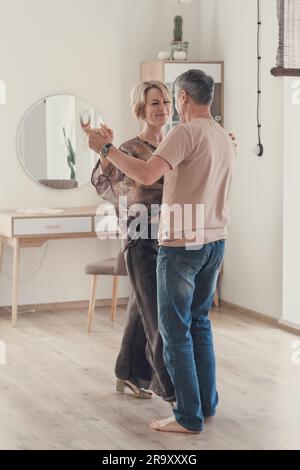 full length shot of middle age couple dancing at home in modern living room. woman and man having fun at home. spending weekend together. celebrating anniversary. Love and relationship Stock Photo
