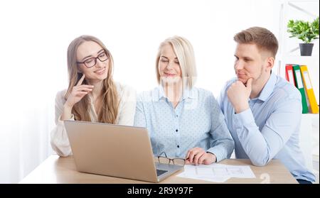 In an office setting, young managers interact with an experienced businesswoman, utilizing a laptop computer for their discussion. Stock Photo