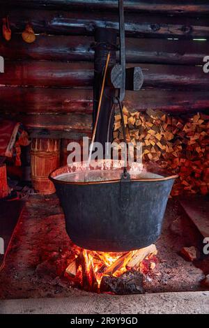 A large vat in which cheese is cooked over an open fire. The black cauldron is prepared over an open wood fire. Cheese factory in the mountains. Stock Photo