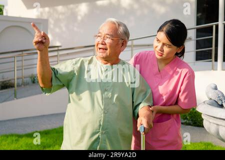 Nurse caregiver helping senior man exercising and walking at hospital or nursing home, Young woman medical worker assisting elderly man at retirement Stock Photo