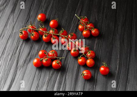 Cherry tomatoes on branches on a dark wooden background, top view. Fresh cherry tomatoes on a textured background. Organic vegetables, veganism. Stock Photo