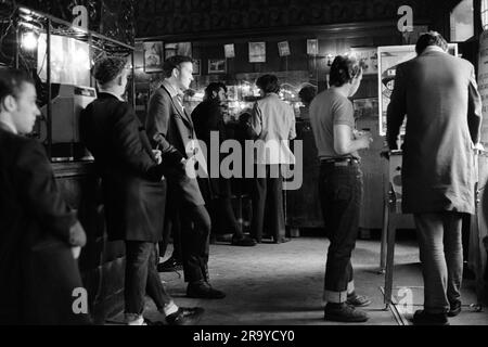 Teddy Boys 1970s. Playing a pinball machine at The Black Raven in Bishopgate Street, a group of Teddy Boys in long drape coats hang out. Moorgate, London, England circa 1975. 1970s UK HOMER SYKES Stock Photo