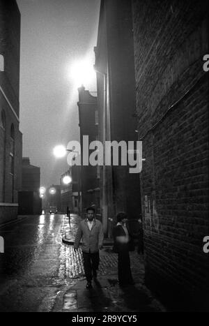 Victorian Slum Buildings East End London 1970s, Brick Lane at the junction with Sheba Street. An Asian man and teenage boy walk past the  Victorian tenement blocks of flats. Tower Hamlets, London, England 1976. 70s UK HOMER SYKES Stock Photo