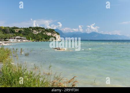 The beautiful shoreline of Sirmione peninsula. The Lido delle Bionde beach and wooden jetty a rocky public beach, Sirmione, Lake Garda, Italy, Europe Stock Photo