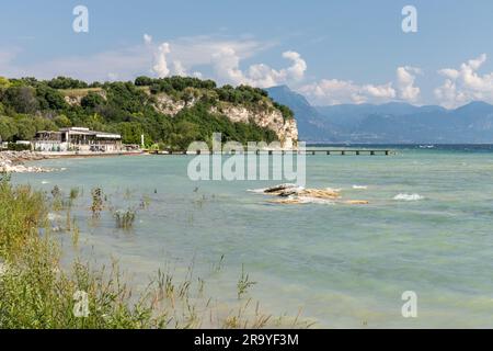 The beautiful shoreline of Sirmione peninsula. The Lido delle Bionde beach and wooden jetty a rocky public beach, Sirmione, Lake Garda, Italy, Europe Stock Photo