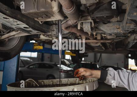 Auto mechanic drains old used engine oil at a service station, scheduled service maintenance of a passenger car Stock Photo