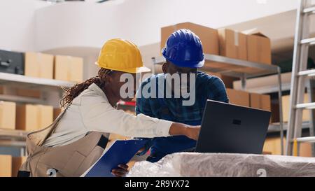 Female supervisor doing quality control in storehouse, working with stock products from warehouse racks. Team of employees checking merchandise for delivery service. Handheld shot. Stock Photo