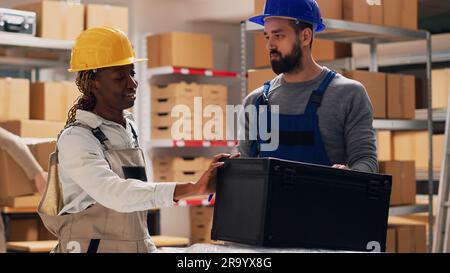 Multiethnic team of people examining list of products on files, talking about merchandise stock for inventory. Man and woman in overalls checking goods in storage room depot, industrial work. Stock Photo