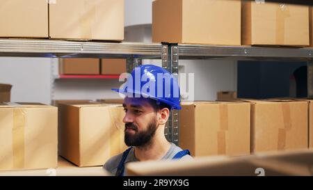 Storehouse employee using scanner on shelves and racks, scanning barcodes on cardboard boxes and checking goods. Male worker checking stock inventory and logstics, industrial distribution. Stock Photo