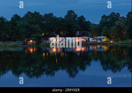 Illuminated tents and caravans at a campsite with waterfront in foreground at night, Småland, Sweden Stock Photo