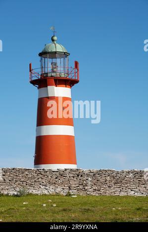 Low angle view of a lighthouse across a short stone wall and against clear blue sky. Gotland island, Sweden Stock Photo