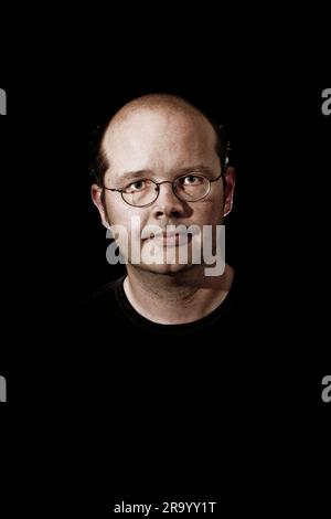 Close-up portrait of a serious mature man in black t-shirt wearing glasses over black background Stock Photo