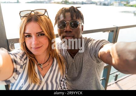 multiethnic couple having fun taking a selfie with smartphone - summer vacation concept on a boat sailing on a river Stock Photo