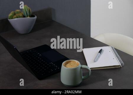 Workspace with a black laptop, blank notebook and green cup of coffee Stock Photo