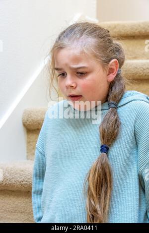 Portrait of a very unhappy 7 year old girl sitting on a staircase. (MR) Stock Photo