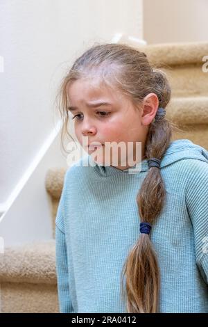 Portrait of a very unhappy 7 year old girl sitting on a staircase. (MR) Stock Photo