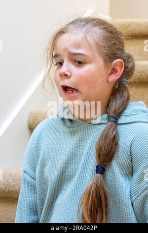 Portrait of a very unhappy 7 year old girl sitting on a staircase. (MR) Stock Photo