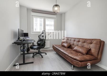 Room with brown leather folding sofa bed and desk with gaming pc or workstation Stock Photo